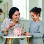 Two daughters watch as mom puts money in piggy bank