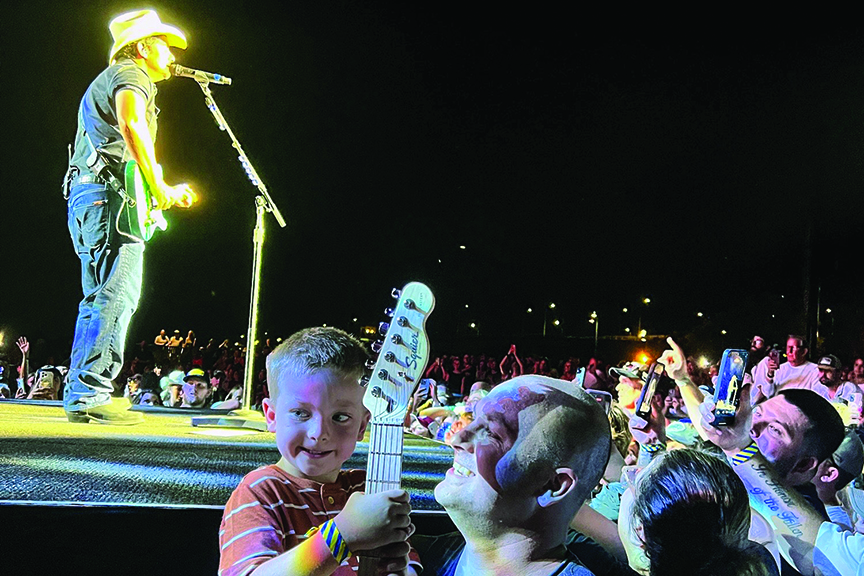 Man with young son holding toy guitar as Brad Paisley performs on stage