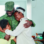 Man in military uniform hugs woman and child