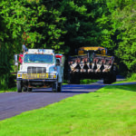 Vehicles haul oversize farm equipment on a residential road