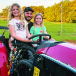 Father and two girls ride on a red tractor