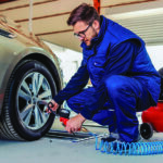 Man checks tire air pressure on front tire of sedan