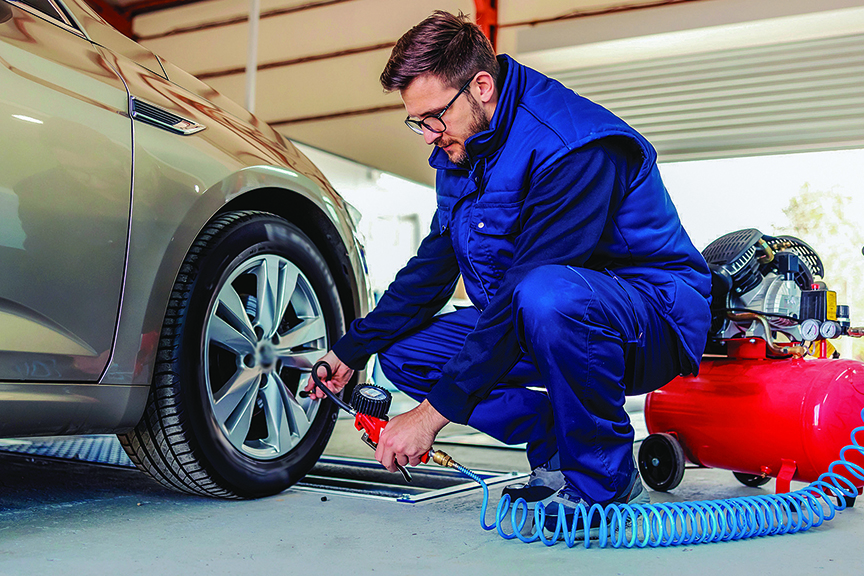 Man checks tire air pressure on front tire of sedan