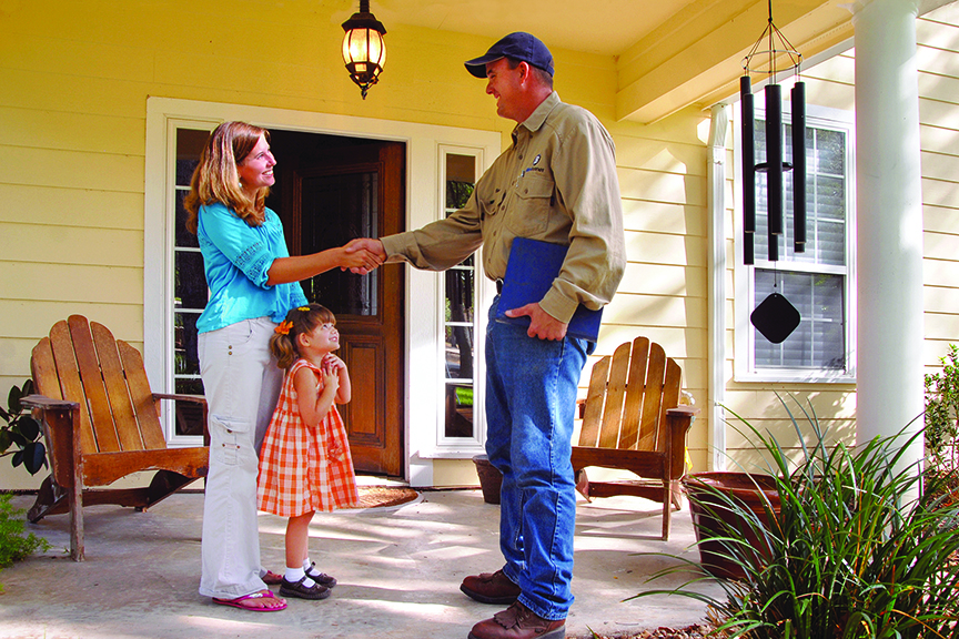 Man and woman shake hands on porch as small child looks on