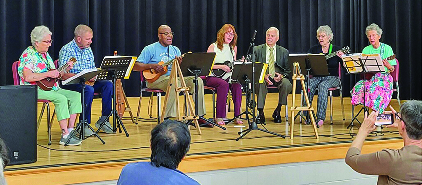 A group plays ukeleles and dulcimers on stage.