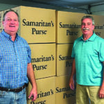 Two men stand in front of Samaritan's Purse boxes