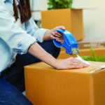 Woman holds packing tape as she tapes a box closed
