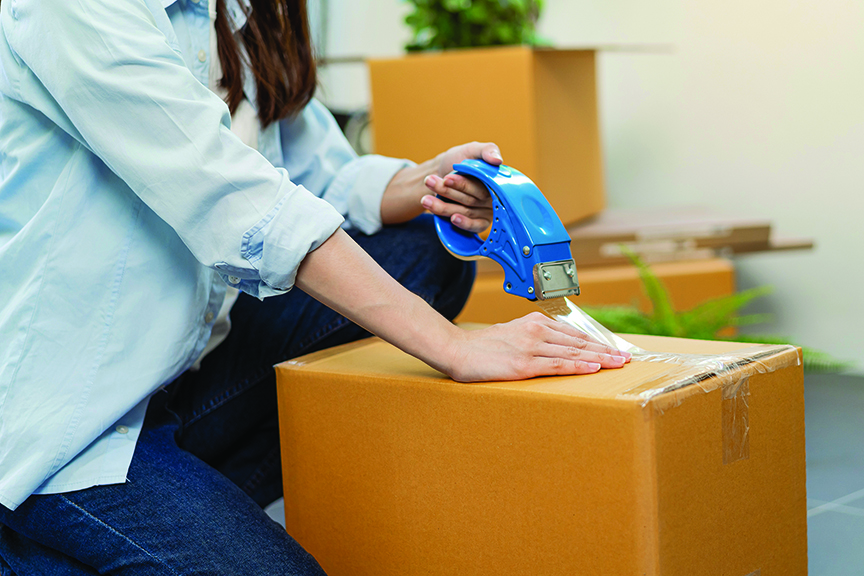 Woman holds packing tape as she tapes a box closed