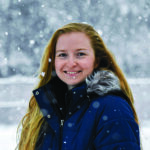 Woman wearing winter coat stands outdoors in the snow.