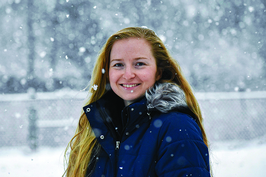 Woman wearing winter coat stands outdoors in the snow.