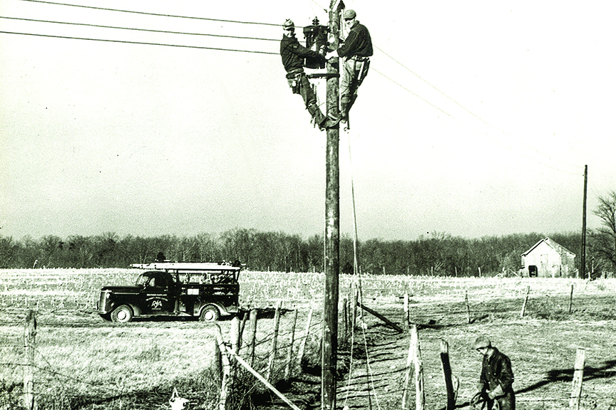 Black-and-white image shows linemen at work in a rural setting