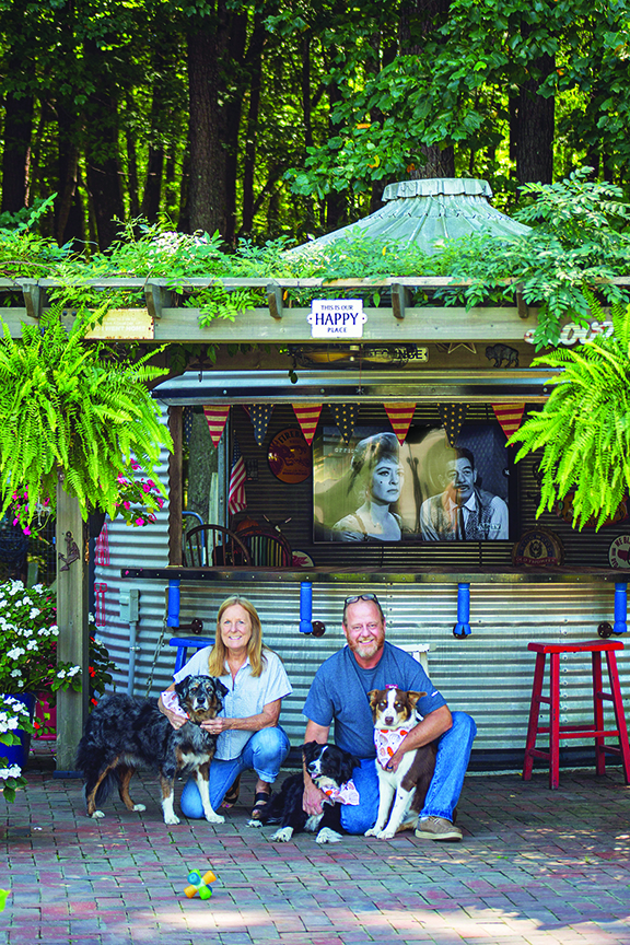 Couple poses with two dogs in front of their backyard “binzebo."