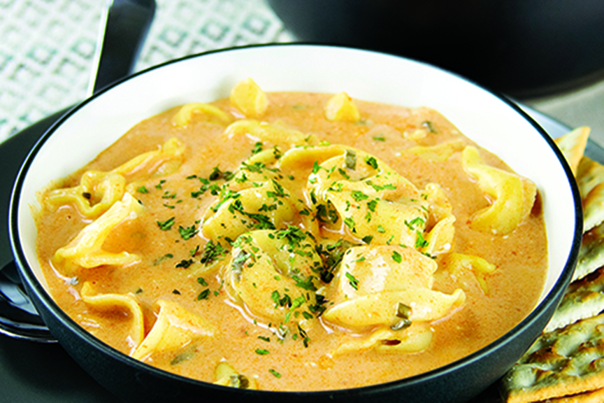 Tortellini soup served in bowl with crackers on the side