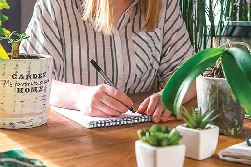 woman surrounded by plants with pen and notepad