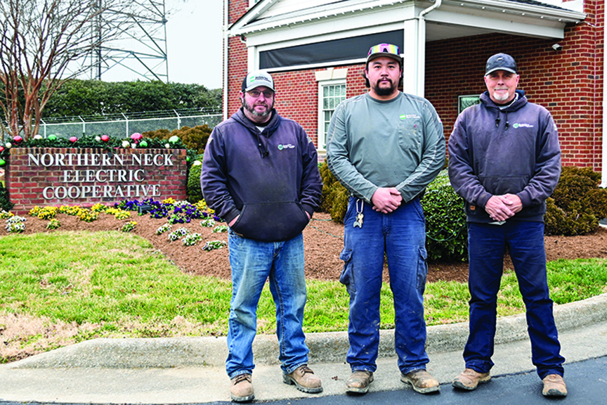 Three lineworkers pose for a photo in front of Northern Neck Electric Cooperative.