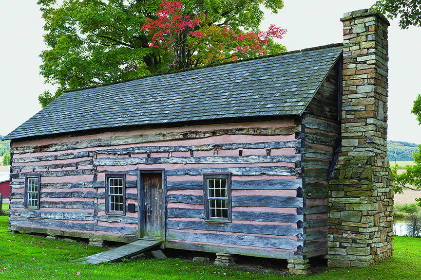 The James Drane House is a rustic, historic log cabin set in a grassy field.