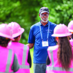 An instructor leads participants wearing pink helmets and vests during VMDAEC's Girl Power Camp, where high school girls explore careers in line work.