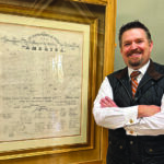 Man poses next to framed, historic copy of the Declaration of Independence