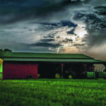 Lightning lights up the sky over farm buildings during a summer storm