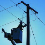 An electric lineman raises clearance on a line on a clear morning.  Silhouette