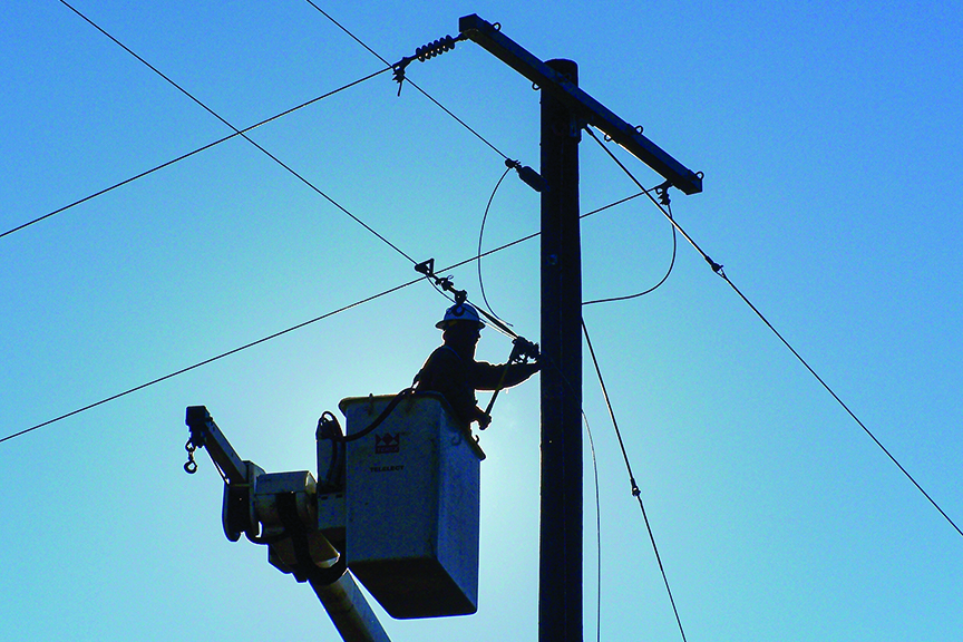 An electric lineman raises clearance on a line on a clear morning.  Silhouette