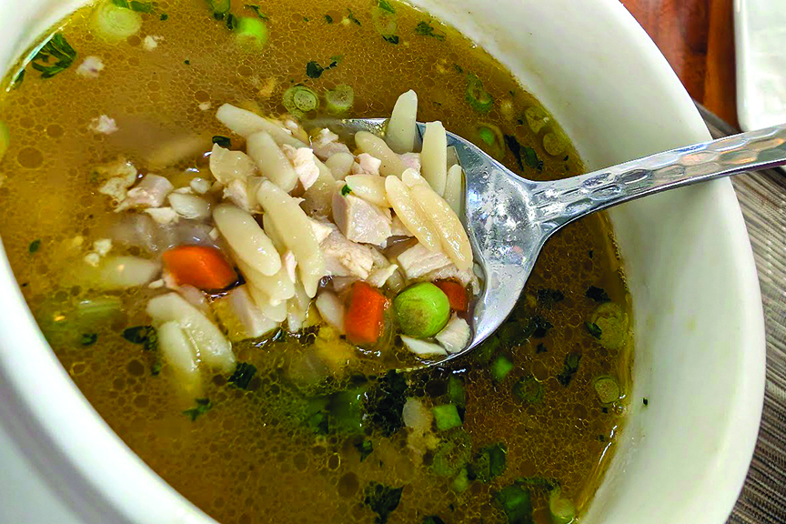 A spoonful of soup containing orzo, fresh vegetables and spring herbs and tender rotisserie chicken