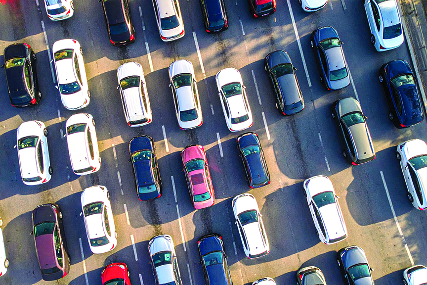 Aerial view of parking lot filled with various cars parked in designated spaces, with some cars casting shadows on ground, showing busy urban environment during daytime