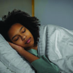 Young woman sleeps on side under white comforter