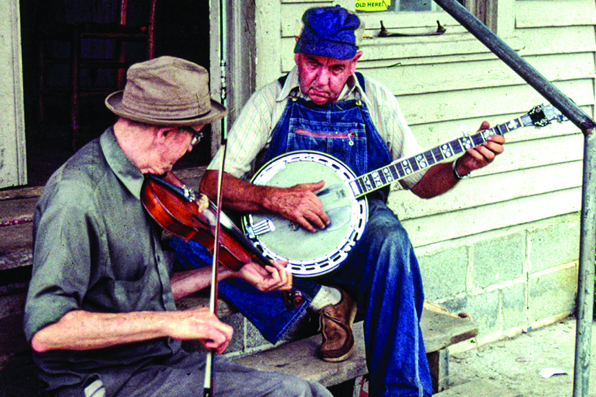 Two musicians sitting on porch steps, one playing a fiddle and the other playing a banjo.