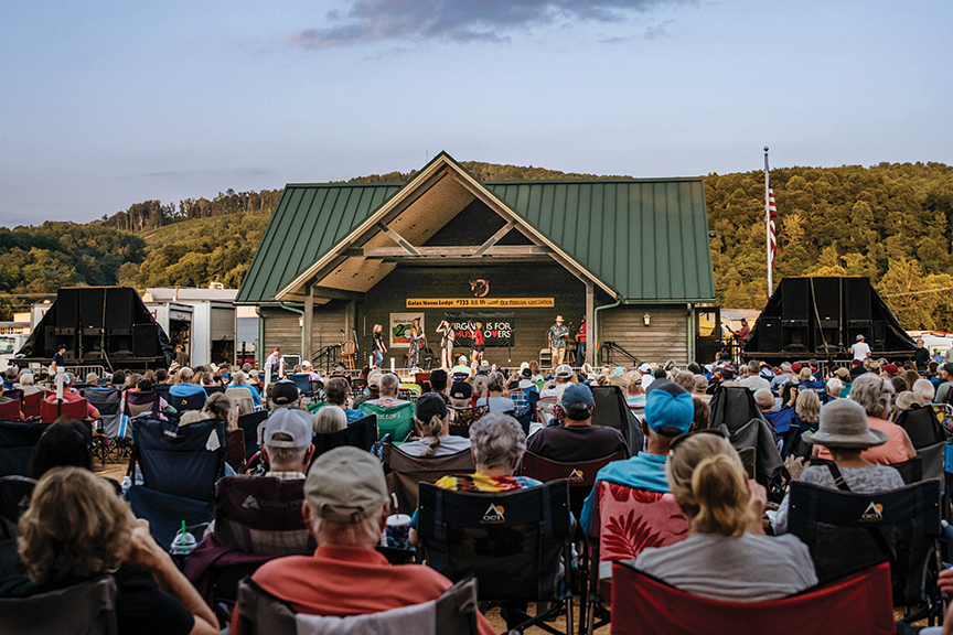A large crowd is gathered to watch musicians perform under a pavilion during the Old Fiddlers' Convention