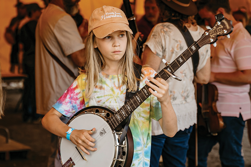 Youngster in orange baseball cap and tie-dye t-shirt plays a banjo.