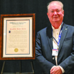 Man stands next to large award plaque