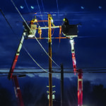 Lineworkers repair power lines from two side-by-side bucket trucks at night.
