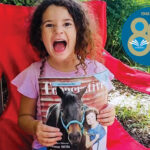 Happy girl holds up issue of Cooperative Living featuring a horse on the cover