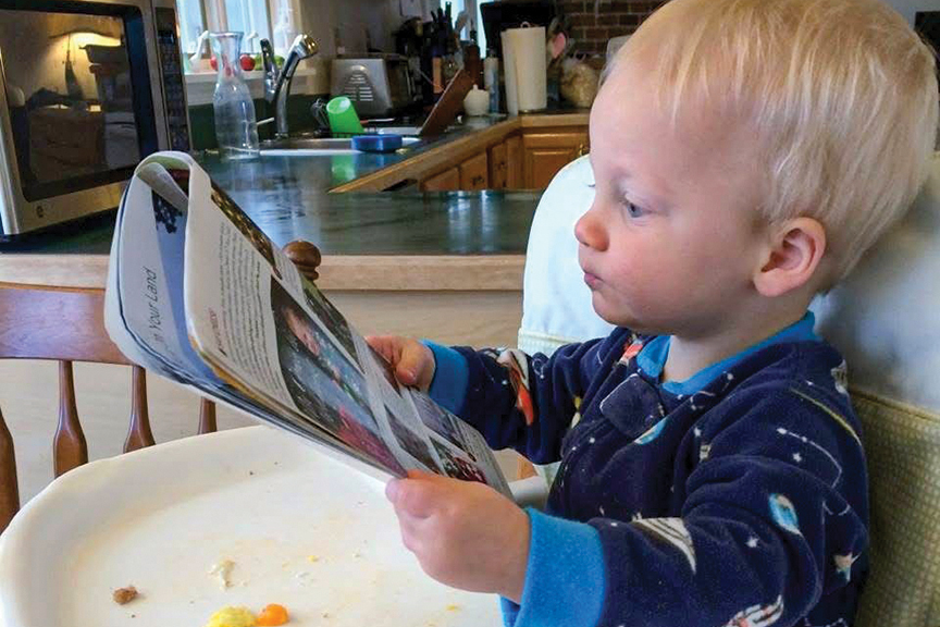 Baby appears to read issue of Cooperative Living at highchair