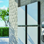 Wall-mounted home battery storage units and an EV charger on a stone exterior wall.