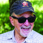 Man wearing a Smokey the Bear baseball cap and sunglasses smiles