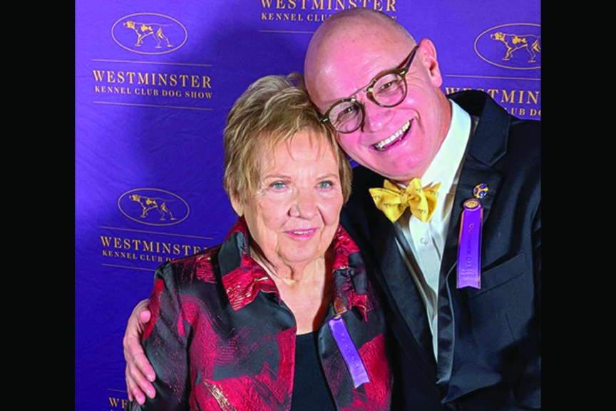 Polly Smith and Michael Faulkner post in front of a purple backdrop emblazoned with the Westminster Kennel Club logo