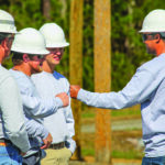 Two men bump fists in group of power line worker trainers and trainees