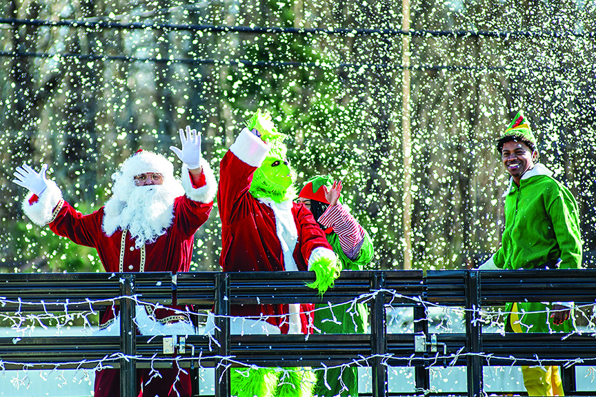 A&N Electric Cooperative employees dressed as Santa, the Grinch, and elves, wave to onlookers as they take part in a community holiday celebration.