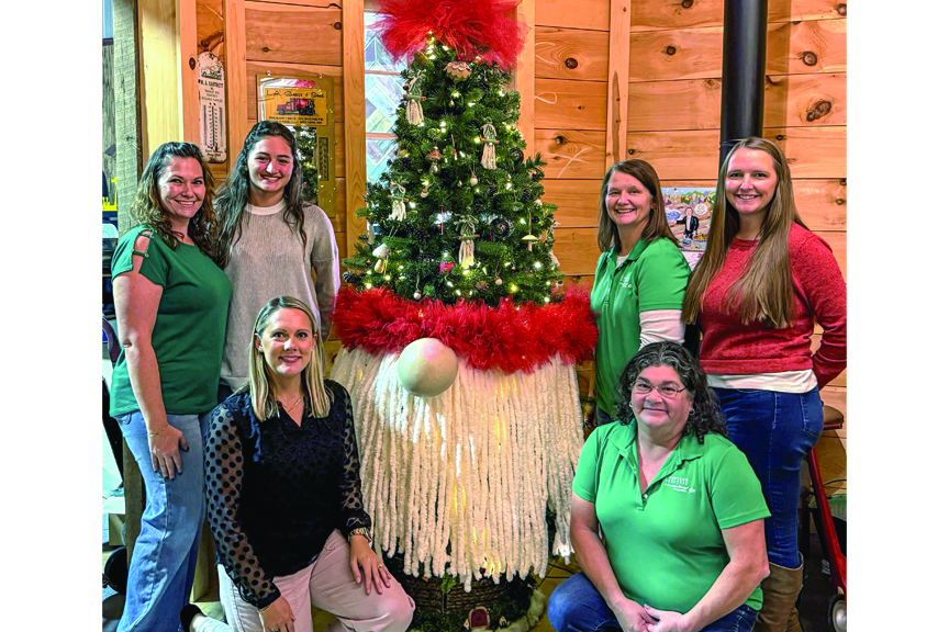 Several women pose around a tree outfitted and decorated to resemble a holiday gnome.