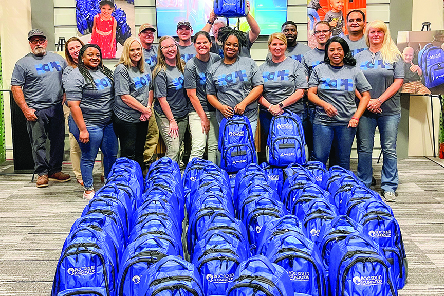 A group of people wearing shirts that read "HOPE" pose with dozens of bags packed for families facing pediatric cancer