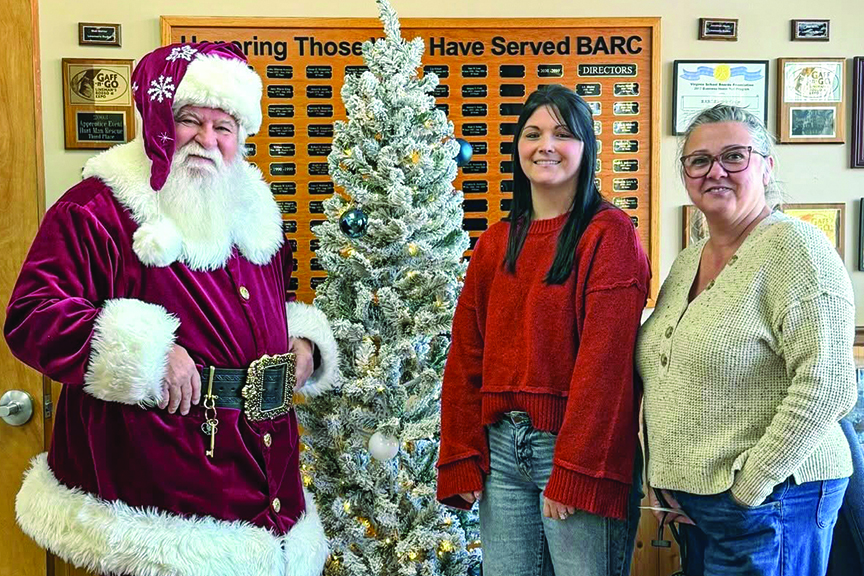 Two BARC Electric Cooperative employees and Santa pose for a photo in front of a Christmas tree.
