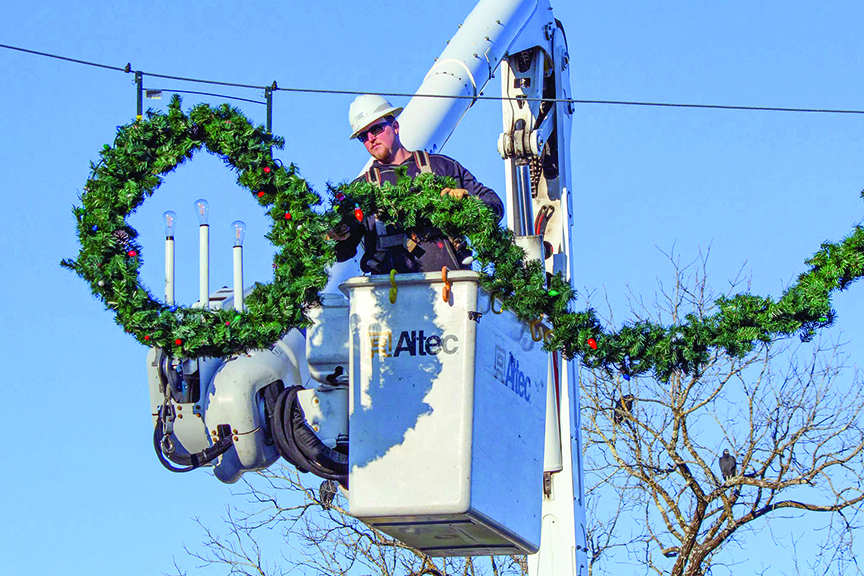 Lineworker in bucket truck hangs greenery and lights