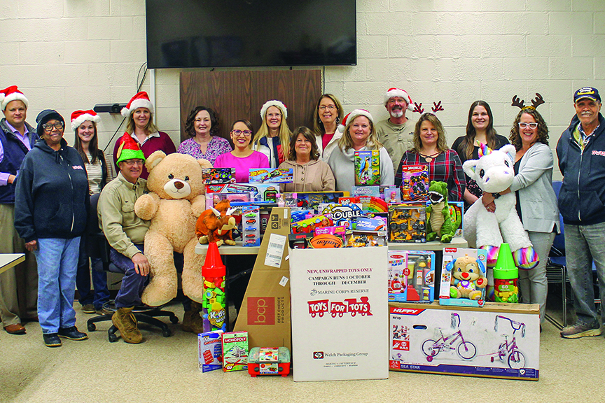 Large group of people pose for a photo with several boxes of toys donated for Toys for Tots