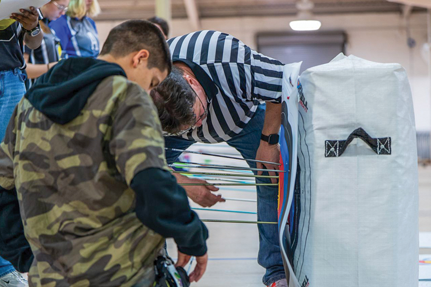 A young man in a camouflage hoodie and a judge inspect a target during an archery competition.